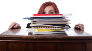 A woman peeking out from behind a stack of folders on a desk.